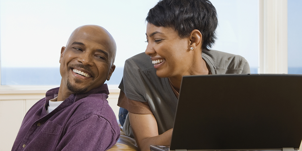 woman at home using laptop and smiling at man sitting next to her