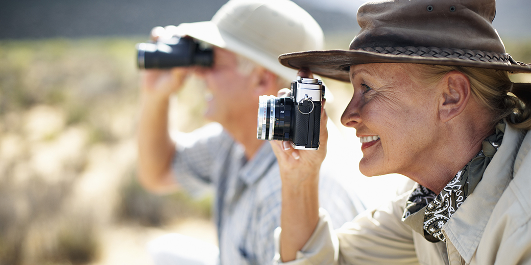 a senior couple wearing safari hats and pointing cameras