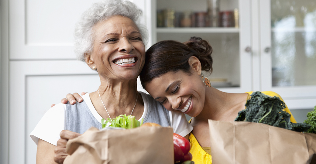 a senior mother with her adult daughter carrying grocery bags in a kitchen