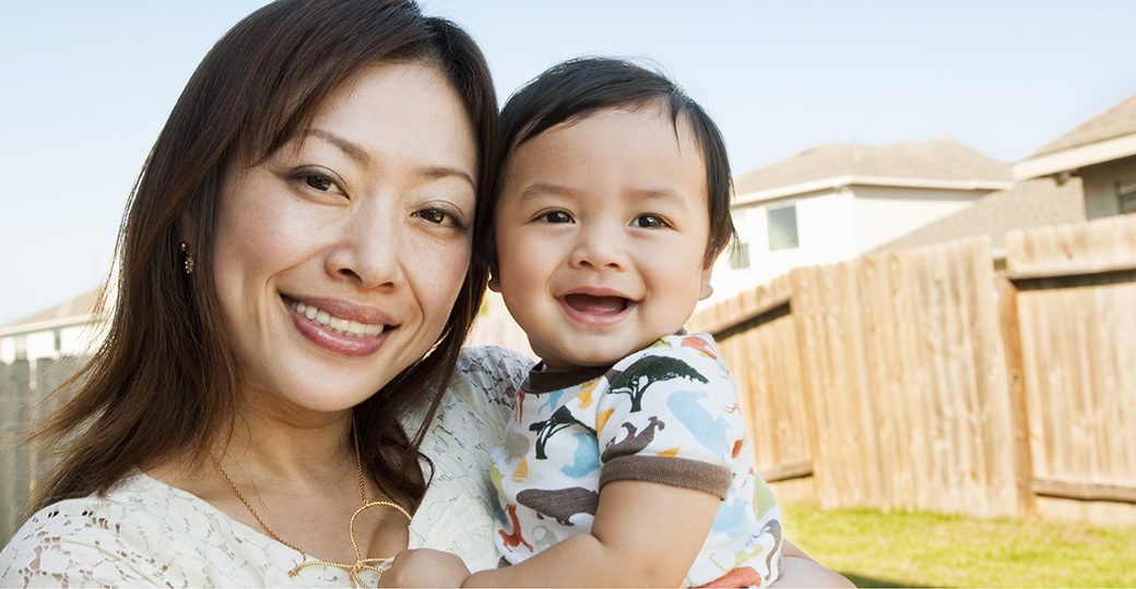 a woman in a backyard carrying a toddler