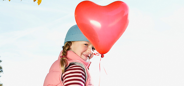 young girl holding heart shaped red balloon