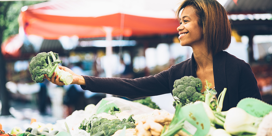 woman holding broccoli at an outdoor market