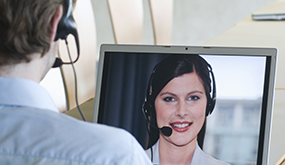 a man wearing a headset and looking at computer screen, on a teleconference with a woman