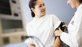 a woman wearing a hospital gown and having her blood pressure measured