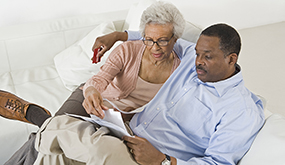a middle aged couple sitting on a couch and looking at documents