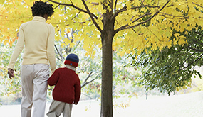 a mother holding a child's hand, and walking in a park