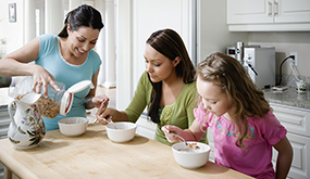 a woman and two girls having cereal at a kitchen counter