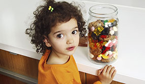 child with jar of candies, looking up at camera