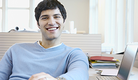 a man sitting next to laptop, facing directly at camera