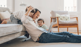 a father sitting on living room floor at laptop, surrounded by playful children