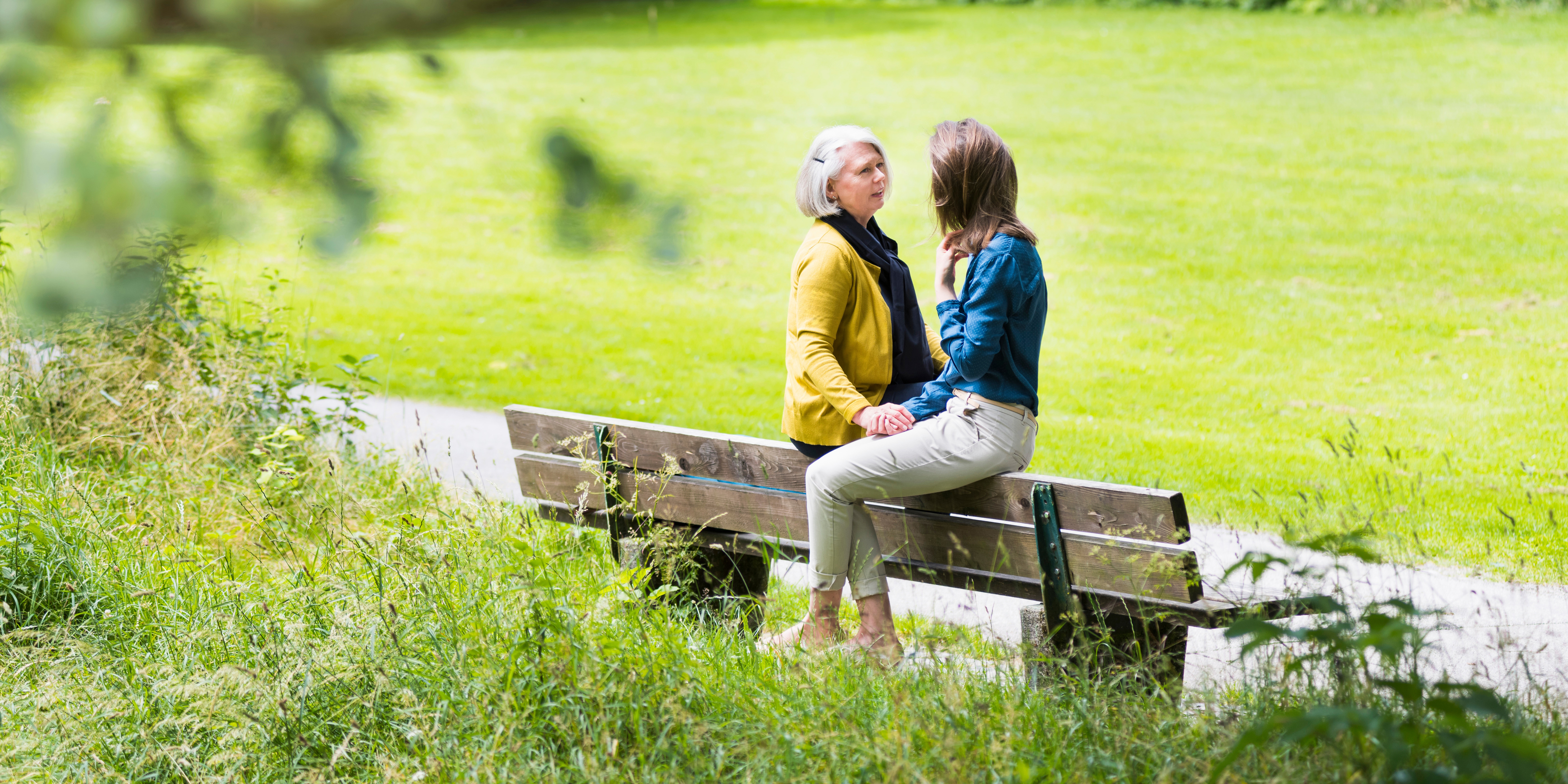 two women talking while sitting opposite on the same park bench