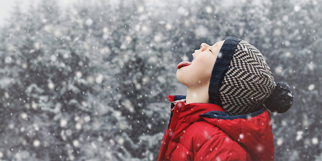 a boy wearing winter clothes opening mouth to catch snow flakes