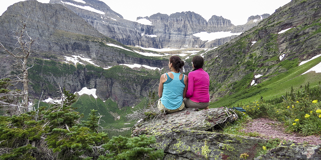 two women sitting atop a view of Glacier Park mountains
