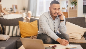 a man working at laptop in living room, and using a cell phone