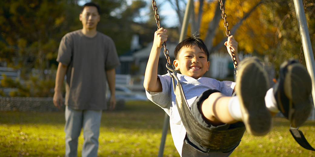 man pushing boy on swing