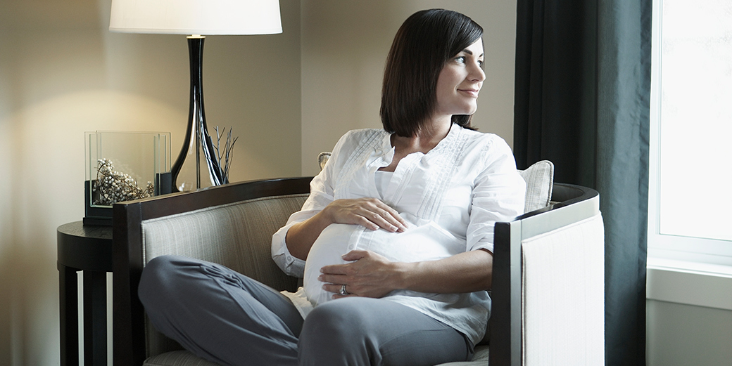 Pregnant woman sitting in living room and looking out a window